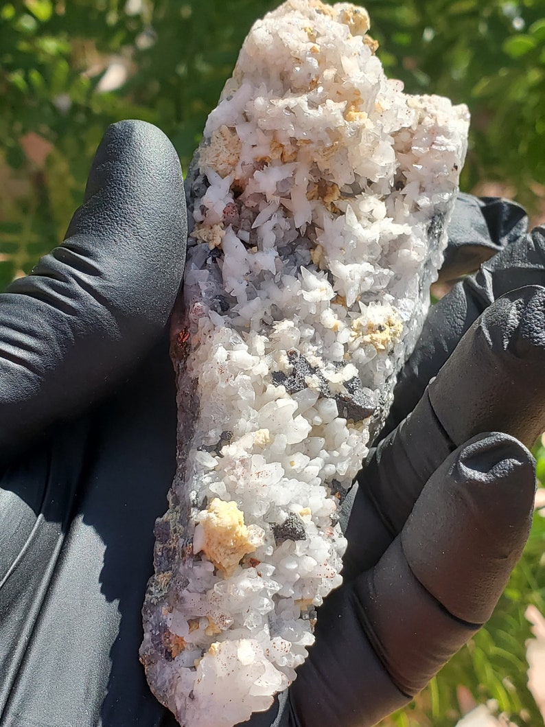 May include: A cluster of white, gray, and brown crystals with a rough, natural texture. The crystals are arranged in a dense, irregular formation.