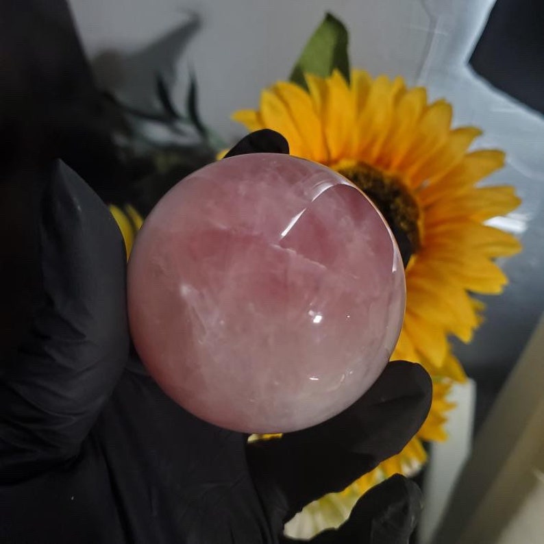 May include: A large, smooth, pink rose quartz sphere. The sphere is polished and translucent, with a light pink hue.