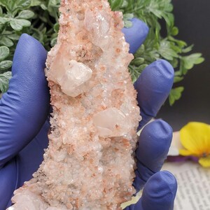 K&ouml;nnte beinhalten: Ein Cluster aus rosa und wei&szlig;en Quarzkristallen mit einer rauen, nat&uuml;rlichen Textur. Die Kristalle sind in einer gezackten, spitzen Formation angeordnet.