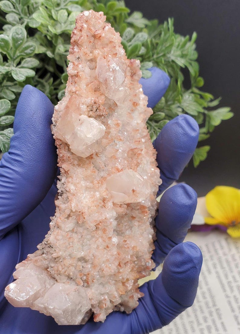 K&ouml;nnte beinhalten: Ein Cluster aus rosa und wei&szlig;en Quarzkristallen mit einer rauen, nat&uuml;rlichen Textur. Die Kristalle sind in einer gezackten, spitzen Formation angeordnet.