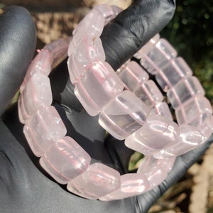 May include: Two pink rose quartz bracelets with square-shaped beads. The bracelets are stacked on top of each other.