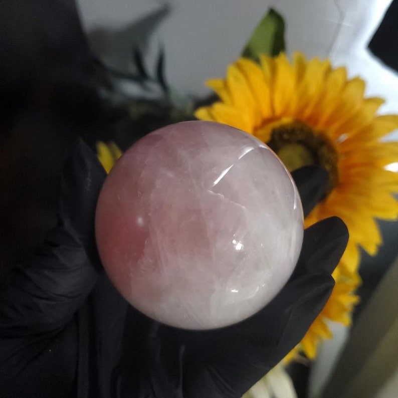May include: A large, smooth, pink rose quartz sphere. The sphere is polished and has a translucent appearance.