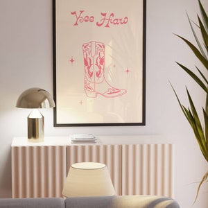 May include: A framed print with a pink cowboy boot illustration and the text "Yee Haw" in a pink cursive font. The print is on a white background with small pink stars.