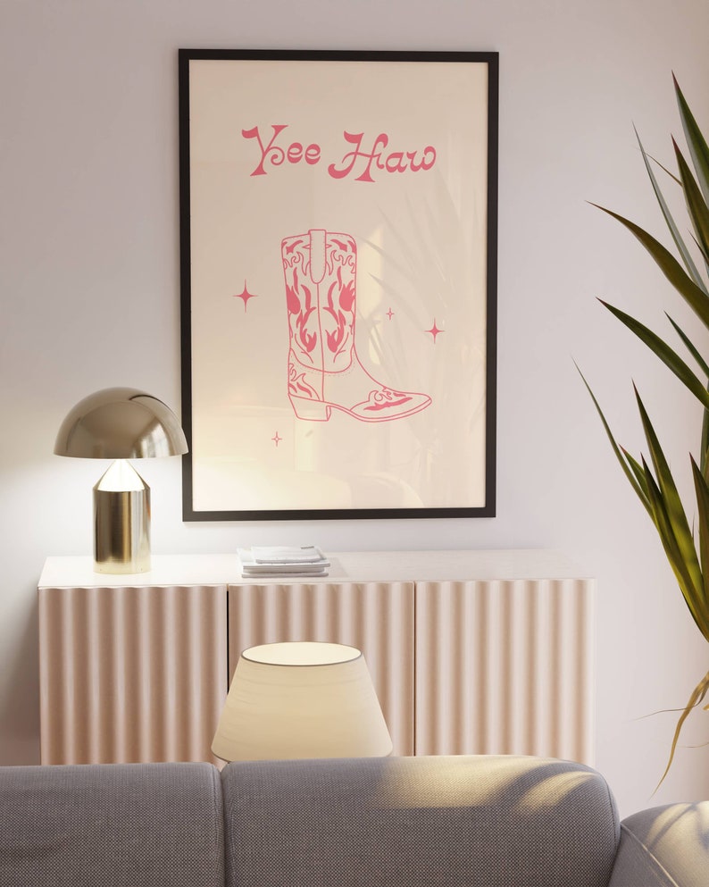 May include: A framed print with a pink cowboy boot illustration and the text "Yee Haw" in a pink cursive font. The print is on a white background with small pink stars.