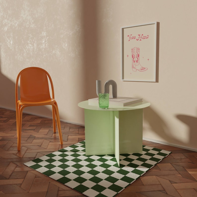 May include: A green checkered rug sits in front of a light green side table with a book and a green glass on top. A bright orange chair sits next to the table. A framed print with the text "Yee Haw" and a pink cowboy boot illustration hangs on the wall.