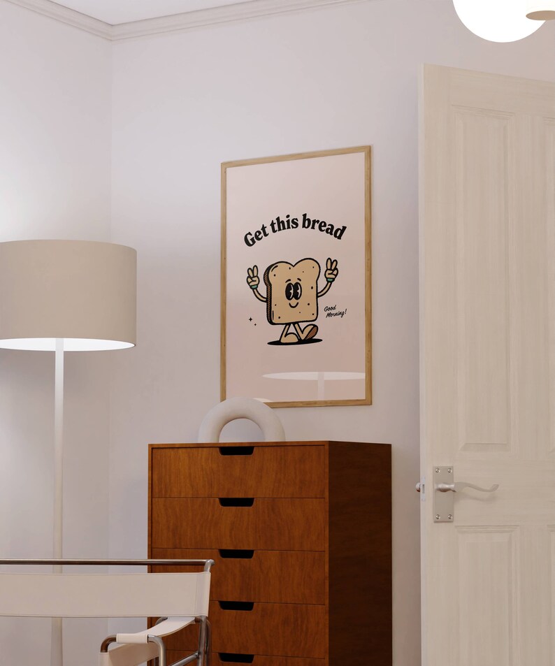 Puede incluir: Una impresi&oacute;n enmarcada con una ilustraci&oacute;n de dibujos animados de una rebanada de pan con brazos y piernas. El pan sonr&iacute;e y hace el signo de la paz con ambas manos. El texto "Get this bread" est&aacute; por encima del pan y el texto "Good Morning!" est&aacute; por debajo del pan.