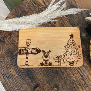 May include: A wooden cutting board with a Christmas theme. It features a reindeer, a Christmas tree, and a sign that says "Nordpol".