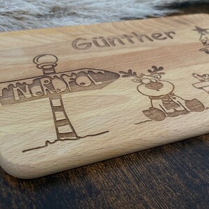 May include: A wooden cutting board with the name "G&uuml;nther" engraved on it. The board also features a cartoon reindeer, a Christmas tree, and a sign that says "Nordpol" (North Pole).