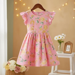 May include: A pink dress featuring a repeating pattern of yellow and orange citrus fruit slices and green leaves. The dress has a round neckline, short flutter sleeves, and a gathered waistline that flows into a full, knee-length skirt.