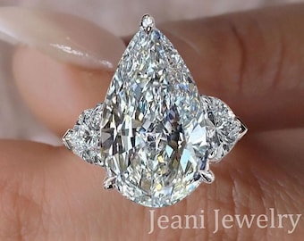 May include: A pear-shaped diamond engagement ring with three prongs on each side. The center stone is a large pear-shaped diamond, and the two side stones are smaller pear-shaped diamonds.