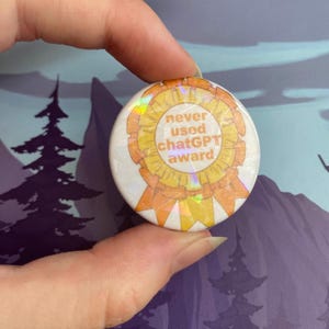 May include: A round, white button with a holographic sheen. The button features a gold and orange award design with the text "never used ChatGPT award". The button is held up by a person's fingers.