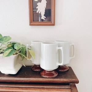 May include: A set of three ceramic mugs with a speckled, matte finish. The mugs are in shades of cream, light gray, and dark gray. Each mug has a simple, modern design and a rounded handle. Perfect for coffee or tea.