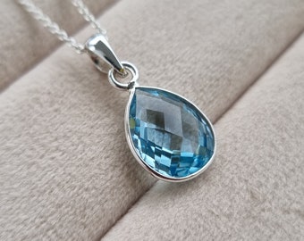 May include: A silver chain necklace with a teardrop-shaped blue topaz pendant.