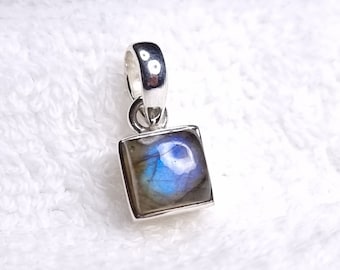 May include: A silver pendant featuring a square-shaped labradorite gemstone. The gemstone displays a blue and grey iridescent sheen.
