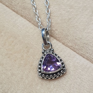 May include: A silver necklace with a triangular pendant featuring a purple amethyst gemstone surrounded by small silver beads.