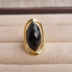 May include: A gold ring with a large, black, faceted gemstone set in a delicate, oval-shaped frame.