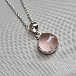 May include: A silver chain necklace with a teardrop-shaped pendant featuring a pale pink gemstone.