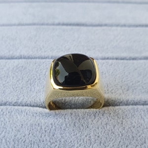May include: A gold ring with a black square-shaped gemstone.