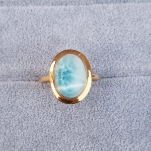 May include: A gold ring with a light blue oval-shaped gemstone. The gemstone has a swirling pattern.