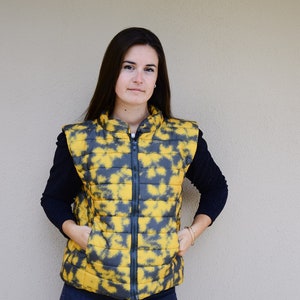 May include: A yellow and gray patterned puffer vest with a zipper closure. The vest is sleeveless and has a stand-up collar.