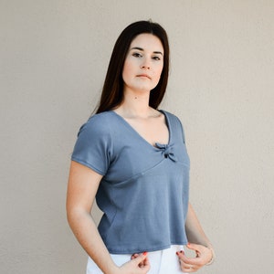 Puede incluir: Una mujer con una blusa azul de manga corta con un detalle anudado en el escote y pantalones cortos de mezclilla blancos.