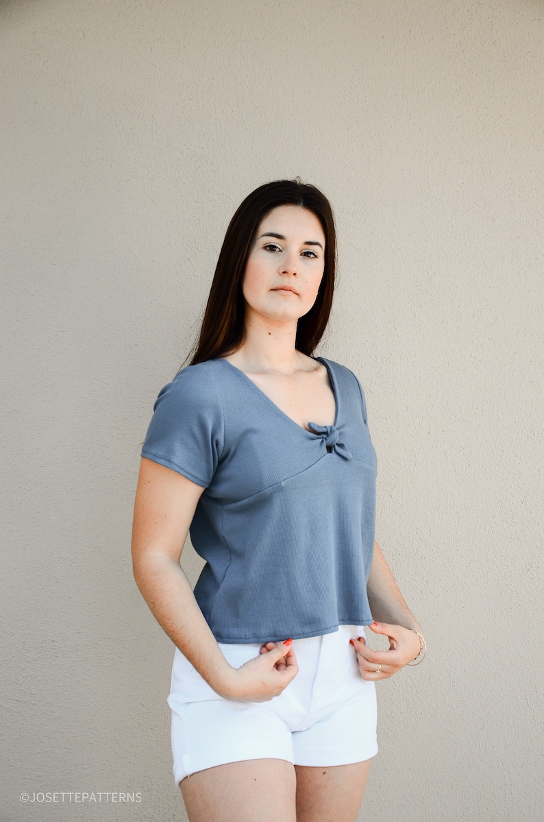 Puede incluir: Una mujer con una blusa azul de manga corta con un detalle anudado en el escote y pantalones cortos de mezclilla blancos.