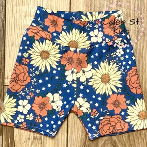 Pode incluir: Shorts azuis com estampa floral com flores laranja, amarelas e brancas sobre um fundo azul com estrelas brancas. Os shorts t&ecirc;m cintura alta e tecido el&aacute;stico.