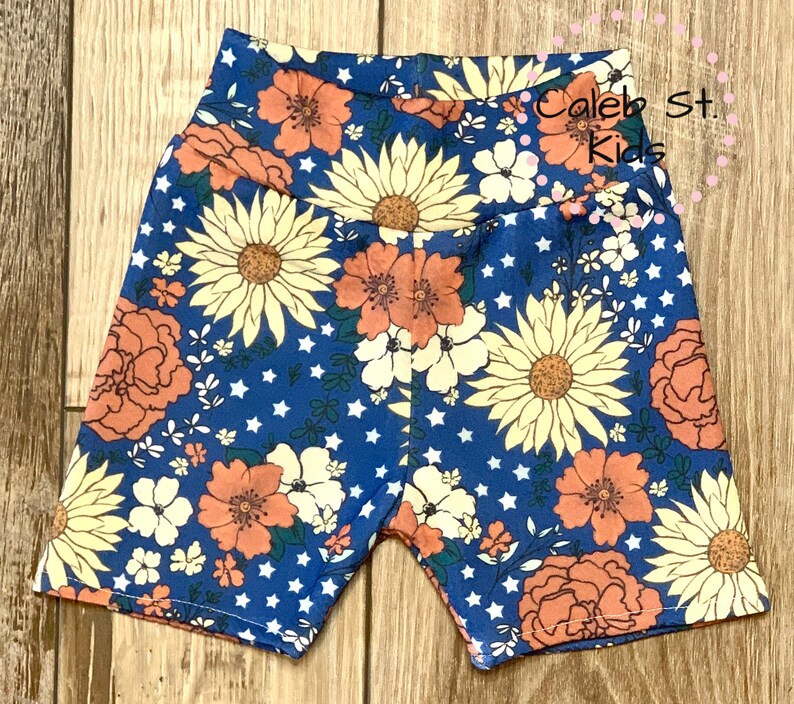 Pode incluir: Shorts azuis com estampa floral com flores laranja, amarelas e brancas sobre um fundo azul com estrelas brancas. Os shorts t&ecirc;m cintura alta e tecido el&aacute;stico.