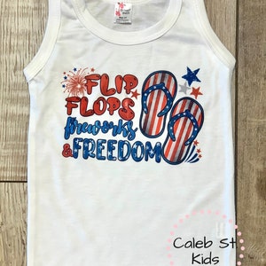 Pode incluir: Camisola branca sem mangas com um gr&aacute;fico vermelho, branco e azul que diz "Flip Flops, Fireworks & Freedom". O gr&aacute;fico inclui um par de chinelos com um design de bandeira americana e fogos de artif&iacute;cio.