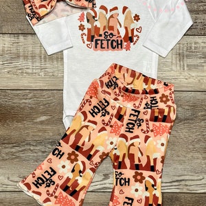 May include: A white long-sleeve onesie with a Christmas-themed graphic featuring three girls wearing Santa hats and the text "So Fetch". The onesie is paired with pink and orange bell-bottom pants with a repeating pattern of the same graphic.