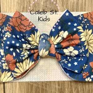 Pode incluir: Uma faixa de cabe&ccedil;a com estampa floral azul e laranja com estrelas brancas. A faixa de cabe&ccedil;a &eacute; amarrada em um la&ccedil;o e &eacute; feita de tecido macio. O texto "Caleb St. Kids" &eacute; vis&iacute;vel na imagem.