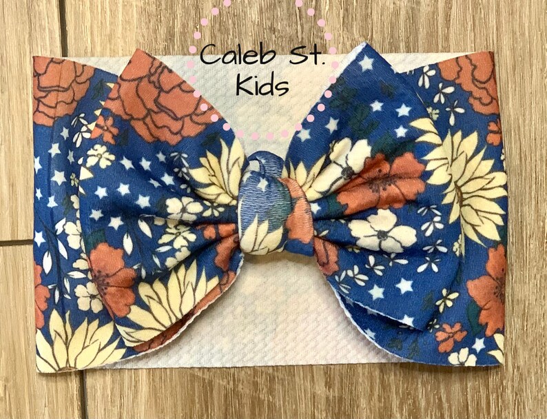 Pode incluir: Uma faixa de cabe&ccedil;a com estampa floral azul e laranja com estrelas brancas. A faixa de cabe&ccedil;a &eacute; amarrada em um la&ccedil;o e &eacute; feita de tecido macio. O texto "Caleb St. Kids" &eacute; vis&iacute;vel na imagem.