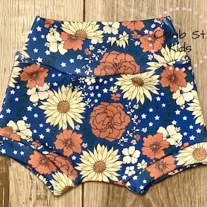 Pode incluir: Bloomers de beb&ecirc; com estampa floral azul e branca com estrelas brancas. Os bloomers t&ecirc;m uma cintura el&aacute;stica e s&atilde;o feitos de um tecido macio e confort&aacute;vel.