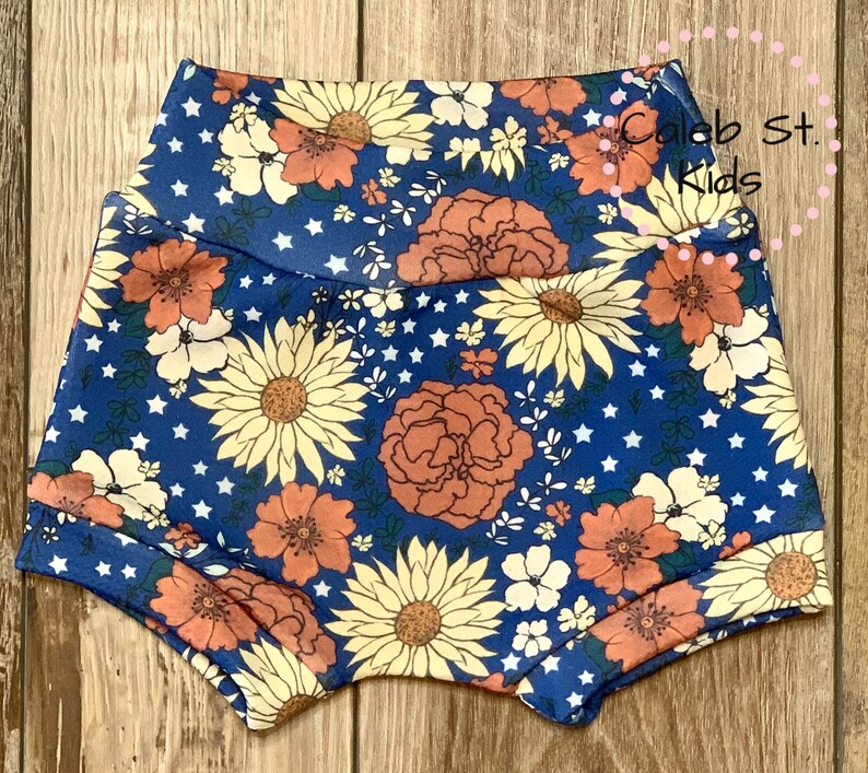 Pode incluir: Bloomers de beb&ecirc; com estampa floral azul e branca com estrelas brancas. Os bloomers t&ecirc;m uma cintura el&aacute;stica e s&atilde;o feitos de um tecido macio e confort&aacute;vel.