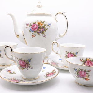 Può includere: Servizio da tè in porcellana bianca con teiera, tazze, piattini e una ciotola. Ogni pezzo è decorato con rose rosa, fiori blu e finiture dorate. Il set è progettato per servire il tè.