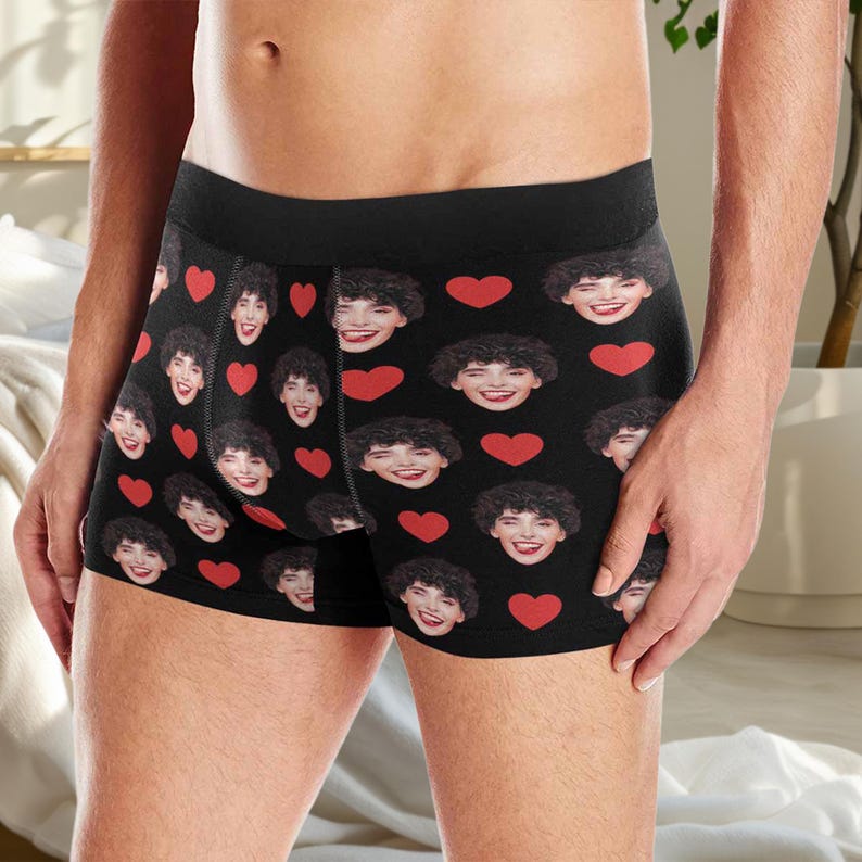 May include: Black boxer shorts with a repeating pattern of a person's face and red hearts.