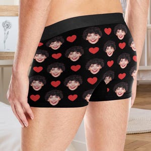 May include: Black boxer shorts with a repeating pattern of red hearts and a person's face.