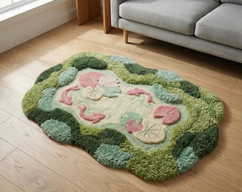 Könnte beinhalten: Ein getufteter Teppich in Form eines Teichs mit rosa Koi-Fischen, Seerosen und einem hellgrünen und cremefarbenen Farbschema. Der Teppich hat ein strukturiertes, weiches Aussehen und ist von Grüntönen umgeben.