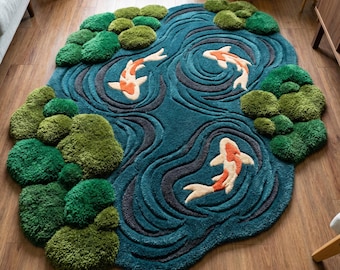 Könnte beinhalten: Türkisfarbener Teppich im Koi-Teich-Design mit unregelmäßiger Form. Der Teppich zeigt drei orange-weiß gestreifte Koi-Fische, die in einem Teich mit dunkelblauen und grauen Wassermustern schwimmen. Grüne, strukturierte Flecken stellen Seerosen dar.
