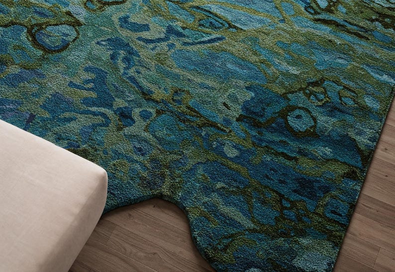 May include: Abstract area rug with a blue and green marbled pattern. The rug has an irregular shape with a curved edge.