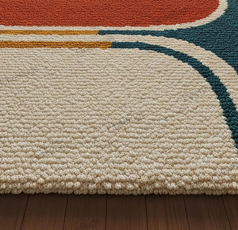 May include: Close-up of a textured rug with a cream-colored background. The rug features a design with orange, yellow, and teal curved lines. The rug is made of a thick, durable material, and is placed on a wooden floor.
