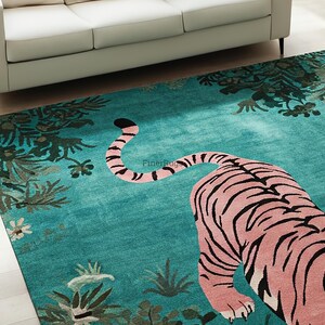 May include: A rectangular area rug featuring a large pink tiger with black stripes centered on a vibrant teal background. The rug displays a botanical pattern of dark green foliage and small flowers along the edges, with the text FinerRugs visible.