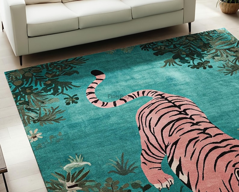 May include: A rectangular area rug featuring a large pink tiger with black stripes centered on a vibrant teal background. The rug displays a botanical pattern of dark green foliage and small flowers along the edges, with the text FinerRugs visible.
