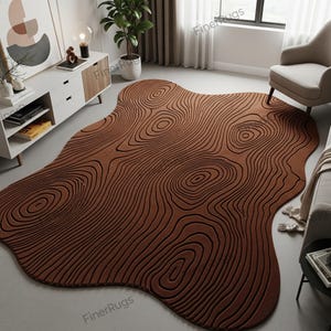 May include: A brown, organic-shaped area rug with a wood grain design. The rug features concentric circles and lines, creating a textured, three-dimensional effect. The rug is a warm, earthy tone, suitable for a living room or bedroom.