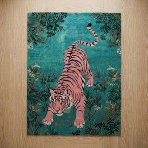 May include: A rectangular area rug featuring a pink tiger with black stripes positioned in the center. The background is a vibrant teal color decorated with dark green foliage, leaves, and small white flowers surrounding the tiger.