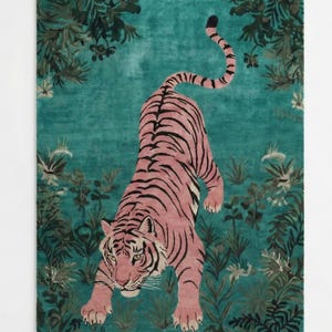 May include: A rectangular area rug featuring a pink tiger with black stripes positioned in the center. The tiger is surrounded by a dark teal background decorated with dark green foliage, leaves, and small white flowers throughout the design.