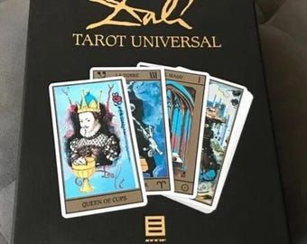 Puede incluir: Un juego de caja negra de la baraja "Dali Tarot Universal". La caja tiene letras doradas y la baraja incluye varias cartas de tarot con ilustraciones coloridas. Una carta está etiquetada como "Queen of Cups".