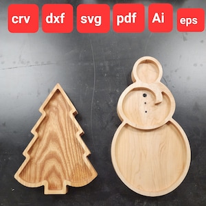 Op de afbeelding: Twee houten serveerschalen, een in de vorm van een kerstboom en de andere in de vorm van een sneeuwpop. Beide schalen zijn gemaakt van lichtbruin hout en hebben een gladde afwerking.