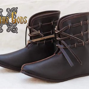 Peut inclure: Paire de bottes en cuir marron avec lacets et sangles. Les bottes ont une pointe pointue et un talon bas.