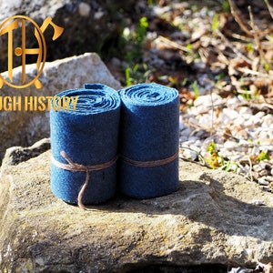 May include: Two rolls of blue fabric, tied with twine, rest on a stone surface. The rolls are tightly wound, showcasing a textured appearance. The image includes the text "THROUGH HISTORY" and a logo.